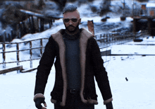 a man with a beard wearing sunglasses and a brown jacket stands in the snow