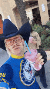 a man wearing a cowboy hat and glasses is holding a drink