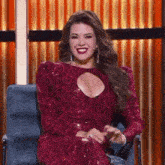 a woman in a red dress is sitting in a chair and smiling at the camera .