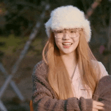 a woman wearing a white fur hat and glasses is smiling .