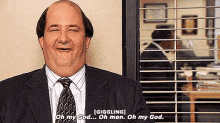 a man in a suit and tie is giggling in front of a window with blinds .