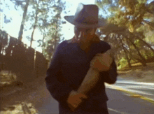 a man in a cowboy hat is walking down a street holding a gun .