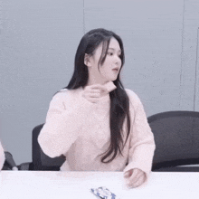 a woman in a pink sweater is sitting at a table with her hands in her pockets .