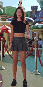 a woman in a crop top and pleated skirt is standing in front of a fence