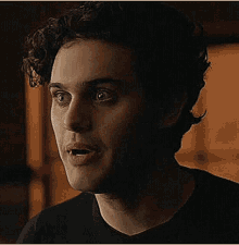 a close up of a man 's face with curly hair wearing a black shirt and smiling .