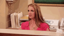 a woman in a pink shirt is sitting at a desk with a phone .
