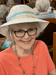 an elderly woman wearing a hat and glasses smiles for the camera