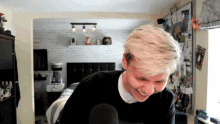 a man in a black shirt is smiling in front of a microphone in a bedroom