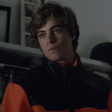 a close up of a young man wearing a black and orange jacket