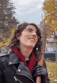 a woman wearing a leather jacket and gloves is holding a large wooden stick