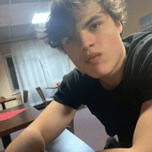 a young man in a black shirt sits at a table in a room