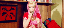 a woman in a pink and red costume is sitting on a bed eating ice cream .