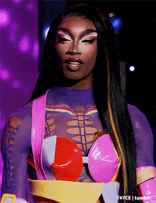 a drag queen is wearing a purple and pink outfit with a yellow belt around her waist