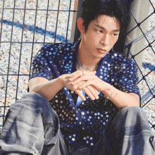 a man wearing a blue shirt with stars on it sits on the ground