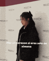 a woman stands in front of a wall that says project m