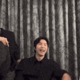 a man in a black shirt is laughing in front of curtains