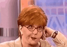 a woman with red hair and glasses is making a funny face with her hand on her head .