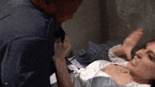 a woman in a hospital gown is laying on a bed with a man in a blue shirt