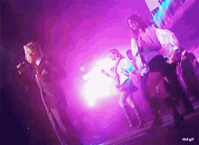 a group of people are dancing and singing on a stage with purple lights behind them