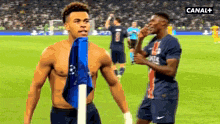 a shirtless soccer player stands next to another shirtless player on a soccer field .