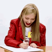 a woman in a red jacket is sitting at a table drawing on a piece of paper .