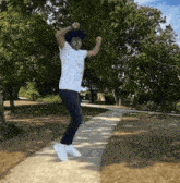 a man in a white shirt is jumping in the air in a park