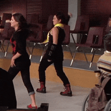 two women are dancing in a room with a man in a wheelchair in the background