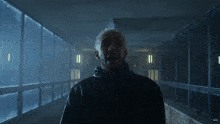 a man in a black jacket is standing in a dark hallway with a window