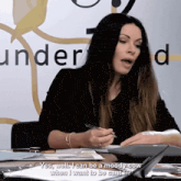 a woman sits at a desk in front of a sign that says " under "