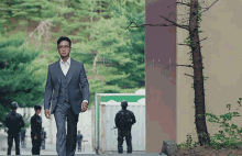 a man in a suit is walking down a street with soldiers in the background