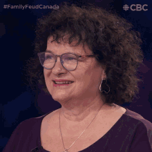 a woman with curly hair wearing glasses and a necklace is smiling in front of a blue background with the letters cbc on it