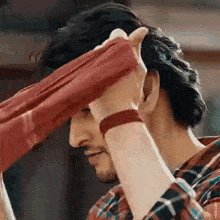 a man in a plaid shirt is holding a red cloth over his head .