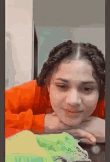 a girl with braids is laying on a table with her head resting on her hands .