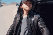 a man wearing a hat and a leather jacket is getting out of a car on a highway .