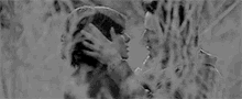 a black and white photo of a man and woman kissing in a field .