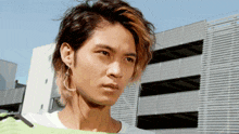 a young man wearing earrings and a green shirt looks at the camera