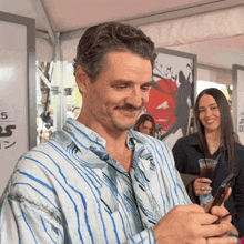 a man in a blue and white striped shirt is holding a cell phone