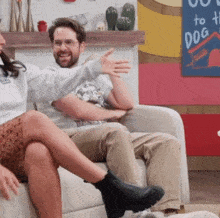 a man and a woman are sitting on a couch in front of a sign that says " out to the dog "