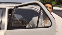 a man is getting out of a white car with a reflection of a person in the window