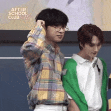 two young men are standing next to each other and one is wearing glasses .