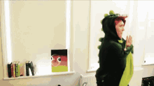 a person in a green dinosaur costume is standing in front of a window