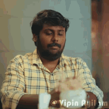 a man in a plaid shirt is sitting at a table with a cup of coffee and the name vipin ayil on the bottom