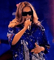 a woman is singing into a microphone wearing sunglasses and a blue dress