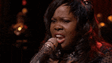 a woman singing into a microphone with a feather headpiece
