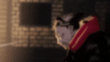 a man in a red jacket is standing in a dark room with a brick wall in the background .