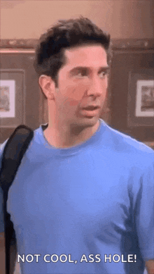 a man in a blue shirt is standing in a room with a backpack .