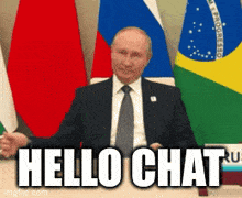a man in a suit and tie is sitting at a table with flags in the background and says hello chat
