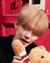 a young man with blonde hair is holding a teddy bear in his hands .