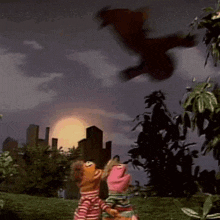 a couple of stuffed animals are standing in a field watching a person flying in the sky