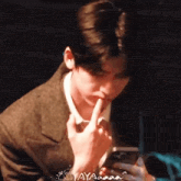 a man in a suit holds his finger to his lips while looking at a cell phone